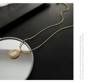 Close-up of mother-of-pearl necklace with gold snake chain and oval stone pendant