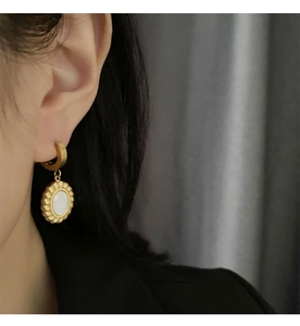 Close-up of golden hoop earrings with mother of pearl pendant worn on ear detail