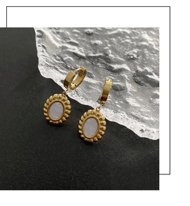 Close-up of gold oval earrings with white mother of pearl inlay on a black textured surface