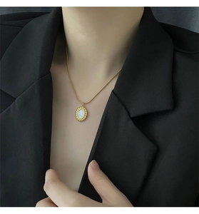 Detail of mother of pearl oval pendant on golden snake chain worn with black blazer