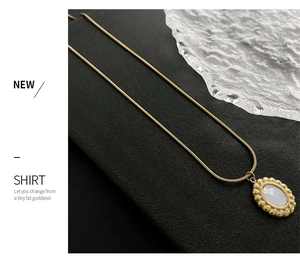 Macro detail of gold snake chain necklace with oval mother of pearl shell pendant