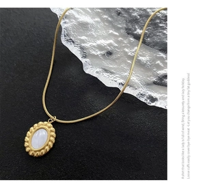 Close-up of vintage gold necklace with white shell pendant on dark textured background