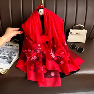 Detailed close-up of red silk scarf with 3D floral embroidery and translucent texture