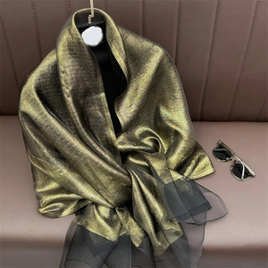 Detail of shimmering gold silk scarf with sheer black mesh border on a leather surface