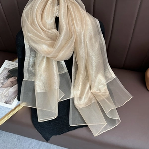Detail of champagne gold shimmering gauze scarf layered on black knitwear