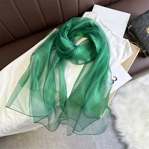 Detail of emerald green thin scarf with metallic shimmering yarn texture on white wood