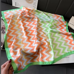 Détail d'un foulard carré en soie avec motifs zigzag verts et orange sur fond en cuir noir