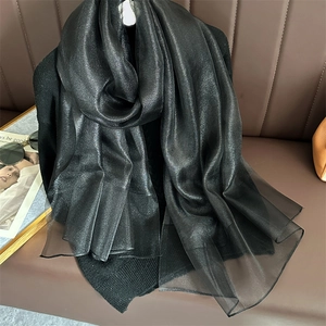 Detail of a black shimmering silk shawl with translucent layers draped on a leather sofa
