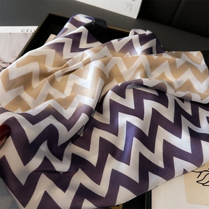 Détail d'un foulard en soie violet et kaki aux motifs zigzag dans un plateau chic