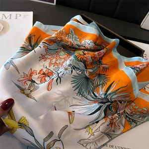 Detailed close-up of tropical leaf and bird print on a glossy silk-textured square scarf