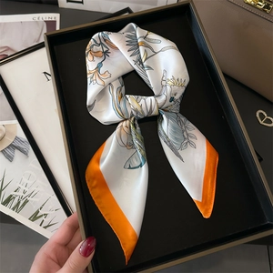 Close-up of bird and flower printed silk scarf on a black tray with stylish fashion items