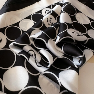 Détail macro de l'imprimé fleur de camélia et pois sur un foulard en satin noir et blanc