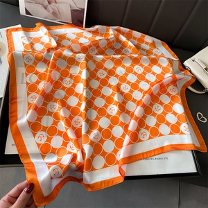 Vue détaillée d'un foulard carré en soie orange avec motifs à pois et roses sur support
