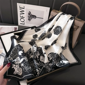 Elegant black and white camellia silk scarf with hand-painted floral print on a leather bag