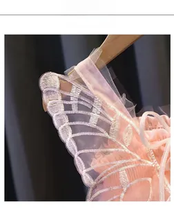 Dettaglio dell'abito da festa in tulle rosa con ricamo a farfalla e spalline a balze