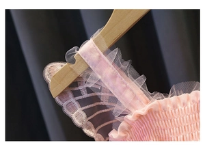 Dettaglio di spalline in rete rosa ricamate e corpetto a punto smock di un vestito bimba