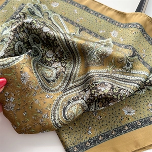 Detail of silk-like square scarf featuring vintage paisley print in mustard and olive green