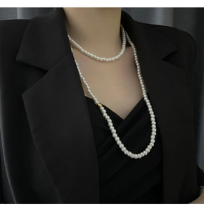 Detail view of long multilayer faux pearl necklace with gold bead on black blazer
