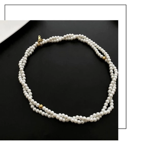 Detail of double-layered pearl necklace with golden beads and clasp on black background
