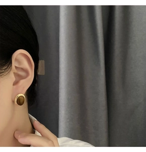 Close-up of vintage golden tiger eye stone earring worn by a model against grey fabric