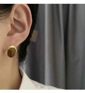 Close-up of vintage oval tiger eye stud earrings with elegant gold metal frame on ear