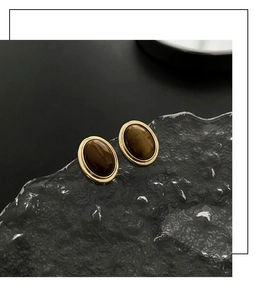 Macro detail of oval tiger eye stud earrings with polished gold-tone metal borders
