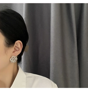 Detail of silver camellia earrings with pavé crystals worn by a model on grey background