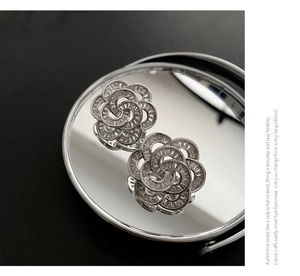 Macro view of silver camellia earrings with pavé crystals on a mirror reflection