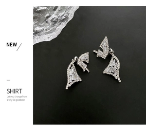 Macro detail of silver wing earrings with pave-set shimmering crystals on black backdrop
