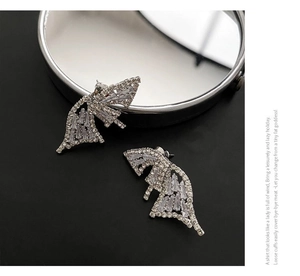 Macro detail of silver geometric butterfly earrings with inlaid cubic zirconia on a mirror