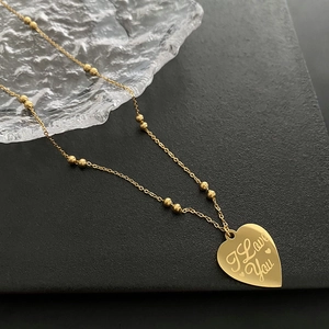 Golden heart necklace with I Love You engraving and beaded chain on a dark tray