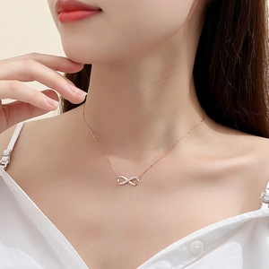 Detail of rose gold infinity necklace with pavé zircons on a model wearing a white shirt