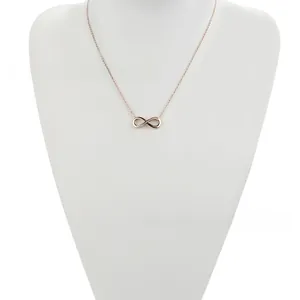 Detail of rose gold infinity pendant with inlaid zircons on a white mannequin