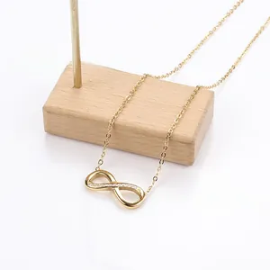 Detailed close-up of a gold infinity pendant necklace with small diamonds on wood base