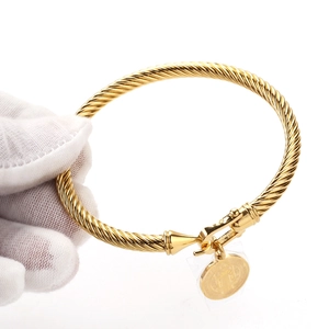 Gros plan d'un bracelet torsadé doré avec fermoir fer à cheval et breloque médaille