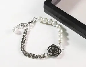 Détail du bracelet en perles et chaîne cubaine avec pendentif camélia sur fond blanc