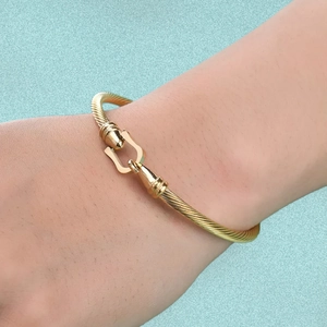 Detail of a gold cable twist bangle featuring a horseshoe shackle clasp on a female wrist