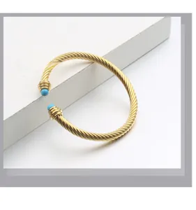 Détail d'un bracelet manchette torsadé doré orné d'embouts en pierres bleues vives