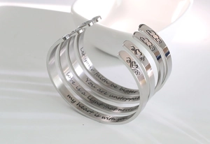 Macro detail of four stainless steel cuff bangles with engraved inspirational quotes
