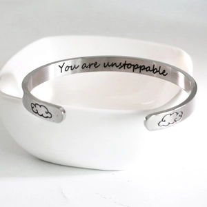 Detail view of engraved You are unstoppable text on C-shaped stainless steel bracelet