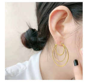 Detail of layered gold titanium steel earrings with textured and smooth concentric rings