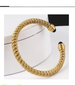 Detailed macro of gold twisted cable cuff bracelet with black bead ends on white stand