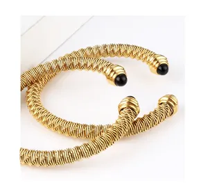Detailed macro view of gold cable twist bangle with black bead tips on a white background
