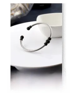 Detailed view of silver cable wire cuff bracelet with black bead accents on white plate