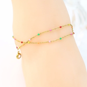 Close-up of double-layer gold anklet with colorful enamel beads and a zircon pendant