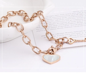 Detail of rose gold link bracelet featuring shell heart pendant and a small key charm