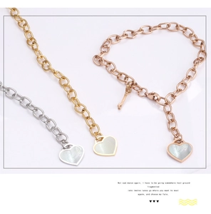 Detail of gold heart pendant with mother of pearl inlay and key charm on steel bracelet