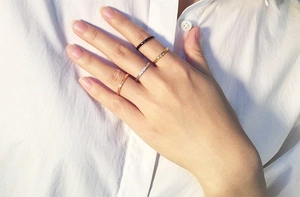 Minimalist stackable steel rings in black, gold, silver, and rose gold on a model's hand
