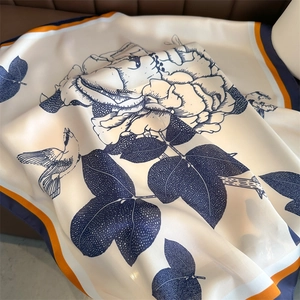 Detailed view of floral silk scarf showing cream fabric with blue peony and bird patterns