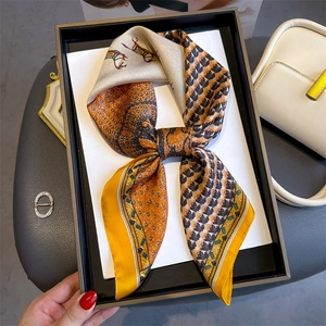 Detail of a silk-feel twilly scarf with horse print tied in a bow inside a gift box